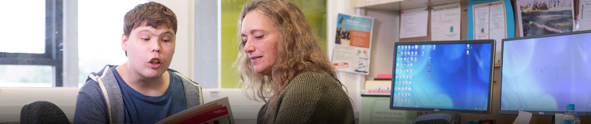 Two people inside an office. They are looking at a book together. Day Programs for people with disability
