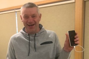 Able client Ross holding an iPhone in his left hand and smiling.