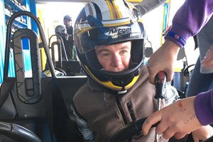 Able client Michael wearing a motorbike helmet being buckled into a go-kart on his holiday.