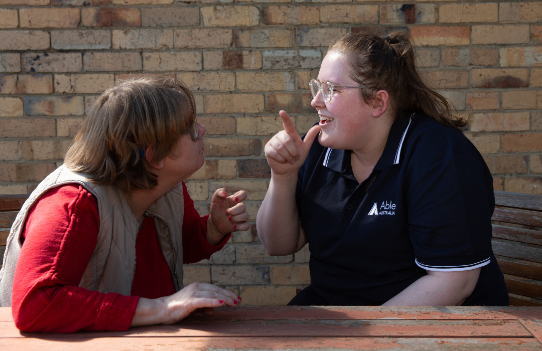 Two peope sitting outside communicating with eachother in Auslan. Support Independent Living, Disability Services