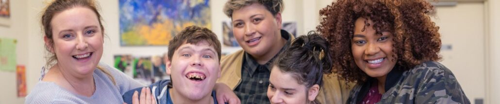 A group photo of five people they are looking at the camera and smiling. They all look really happy. Disability Services.