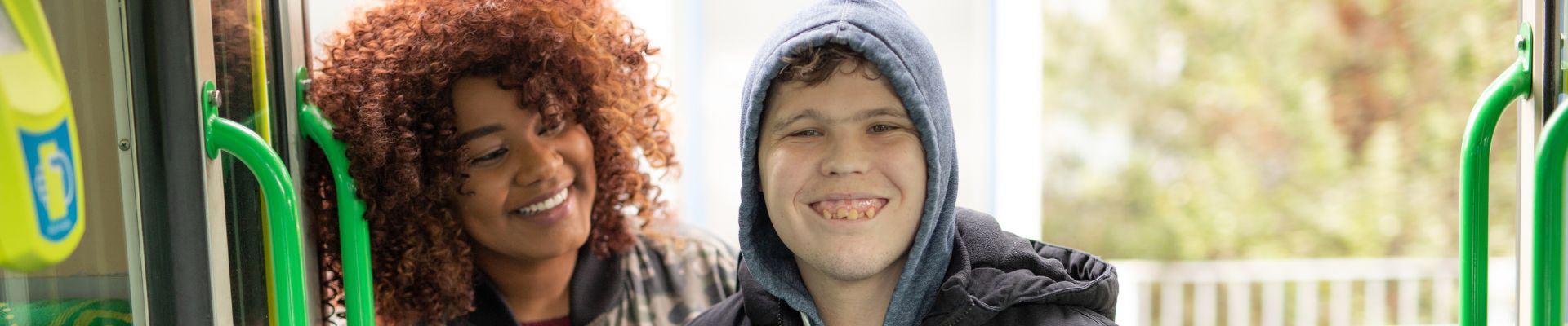 Image of a male getting on a tram he is smiling at the camera and behind him is his support worker who is supporting him and looking at him. Day Programs for adults with disability,