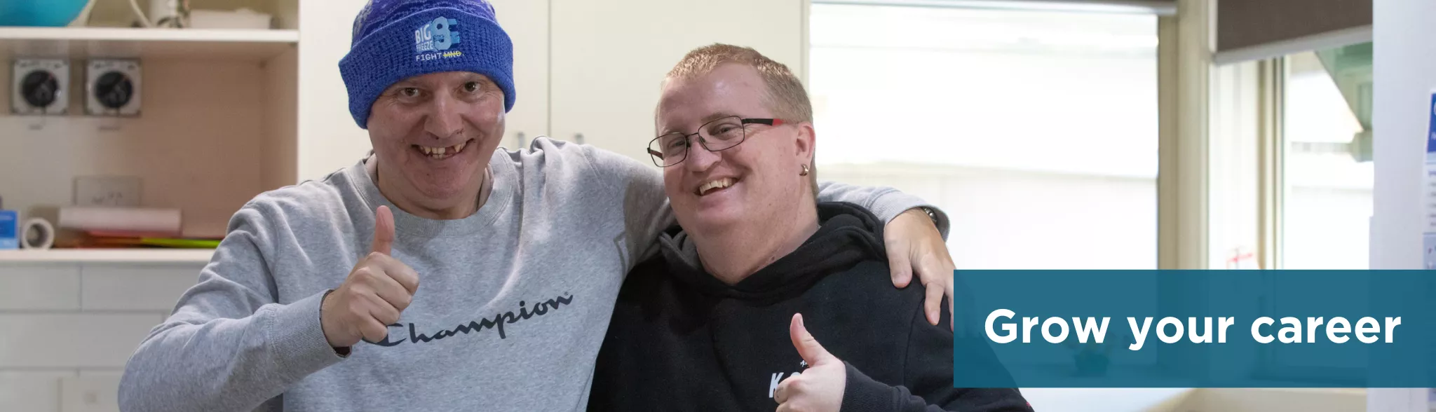 Two people in the kitchen with their arms around eachother smiling at the camera with their thumbs up. Supported Independent Living.