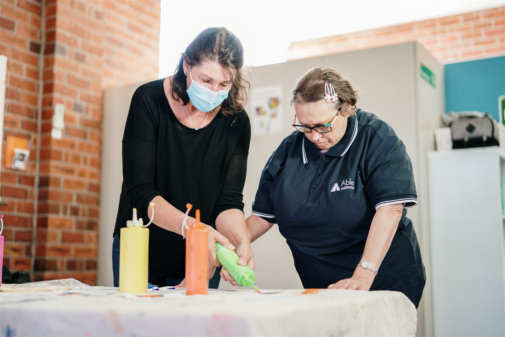 Able Australia support worker guiding a client through a painting activity, fostering creativity and skill development in a safe, inclusive space.